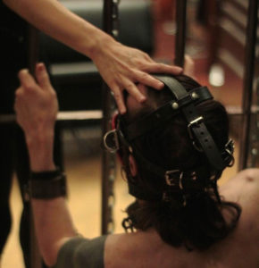 Professional Dominatrix Domina Yuki demands obedience from her male slave bound in a leather mask and leather cuffs.