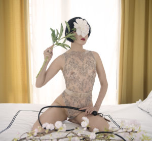 San Francisco and Oakland Asian Dominatrix Domina Yuki framed in a window with a leather whip and flowers.